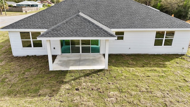 rear view of house featuring a patio, a yard, and roof with shingles