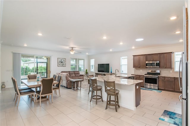 kitchen with appliances with stainless steel finishes, a breakfast bar, decorative backsplash, a kitchen island with sink, and light stone countertops