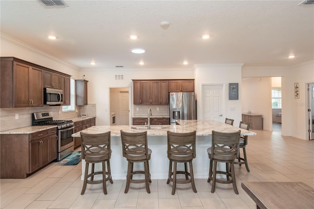 kitchen with sink, a breakfast bar area, a center island with sink, stainless steel appliances, and light stone countertops