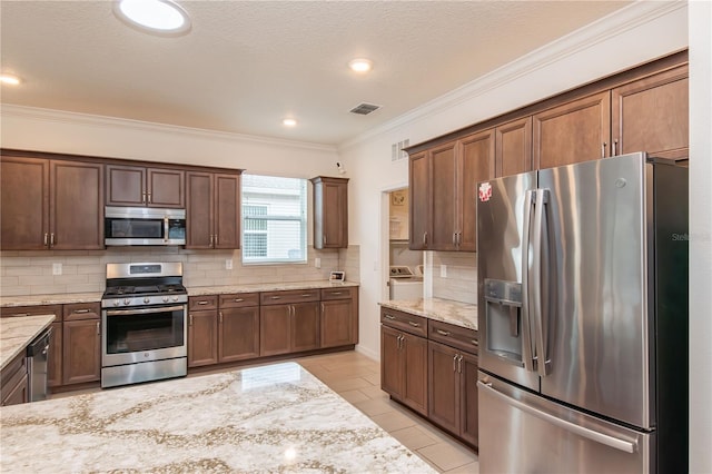 kitchen featuring crown molding, appliances with stainless steel finishes, light stone countertops, washer and clothes dryer, and backsplash