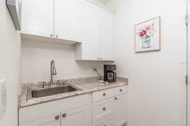 kitchen with light stone counters, sink, and white cabinets