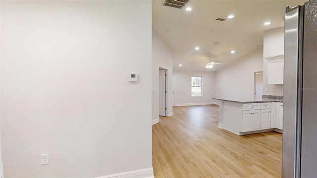 kitchen with stone countertops, white cabinetry, stainless steel fridge, ceiling fan, and light wood-type flooring