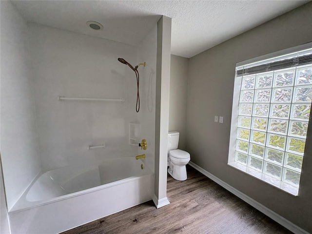 bathroom with hardwood / wood-style flooring, toilet, bathing tub / shower combination, and a textured ceiling