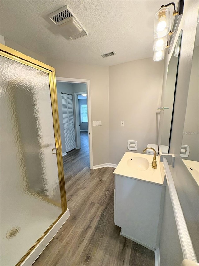 bathroom featuring vanity, wood-type flooring, a shower with door, and a textured ceiling