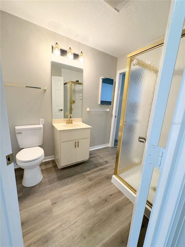 bathroom featuring a shower with shower door, hardwood / wood-style flooring, vanity, toilet, and a textured ceiling