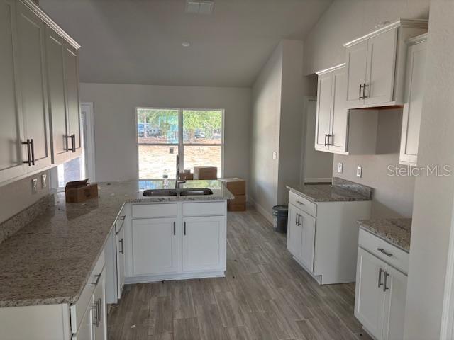 kitchen featuring sink, white cabinetry, light stone counters, wood-type flooring, and kitchen peninsula