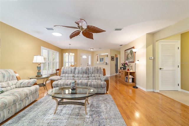 living area featuring light wood-type flooring, baseboards, visible vents, and ceiling fan with notable chandelier