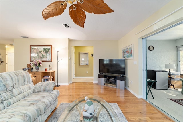 living area with light wood-type flooring, ceiling fan, visible vents, and baseboards