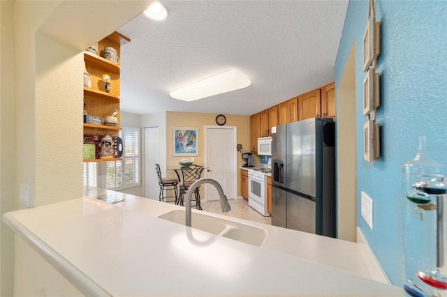 kitchen featuring white appliances, light countertops, a textured ceiling, open shelves, and a sink