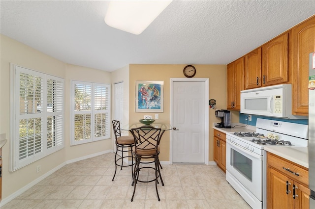 kitchen featuring a textured ceiling, light countertops, white appliances, and brown cabinets