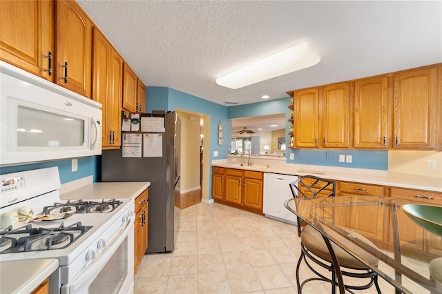 kitchen with a textured ceiling, white appliances, a sink, light countertops, and brown cabinetry