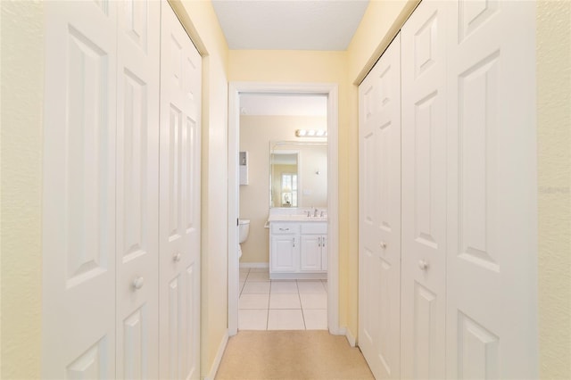 hallway featuring light tile patterned flooring, a sink, and baseboards