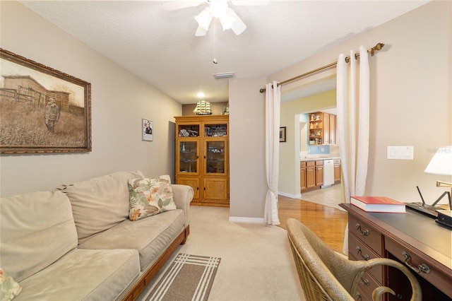 living area with light colored carpet, visible vents, a ceiling fan, a textured ceiling, and baseboards