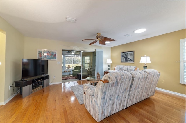 living room with light wood-style flooring, visible vents, baseboards, and a ceiling fan