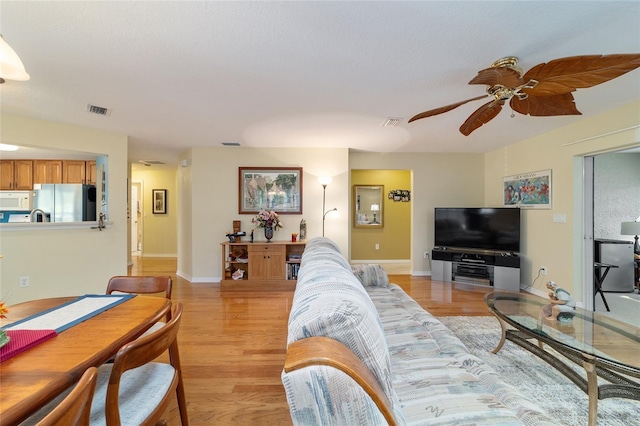 living area featuring a ceiling fan, visible vents, light wood-style flooring, and baseboards