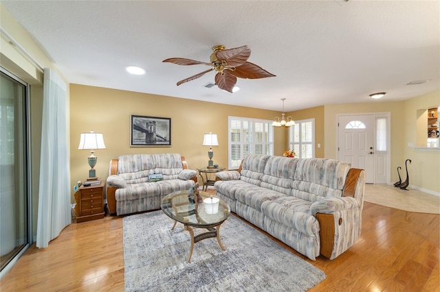 living room with light wood-style floors, visible vents, baseboards, and ceiling fan with notable chandelier