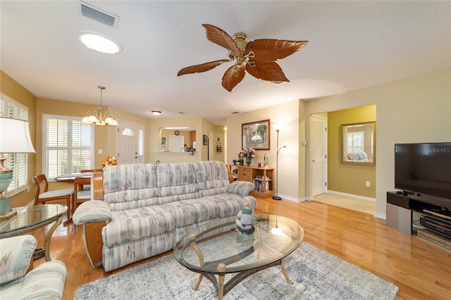 living room featuring light wood finished floors, baseboards, visible vents, and ceiling fan with notable chandelier