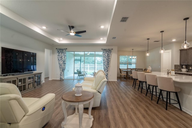 living room with a tray ceiling, wood-type flooring, and ceiling fan with notable chandelier