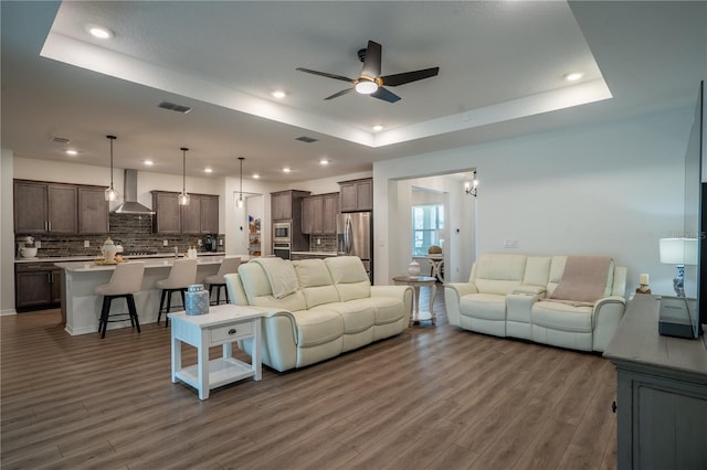 living room with a tray ceiling, dark hardwood / wood-style floors, and ceiling fan