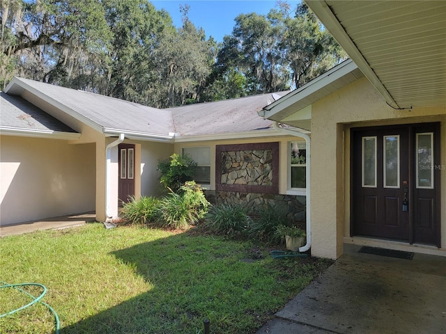 view of exterior entry featuring stucco siding, stone siding, and a yard