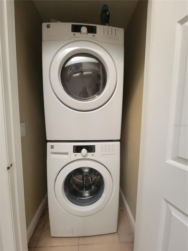 clothes washing area with laundry area, stacked washer / dryer, light tile patterned flooring, and baseboards