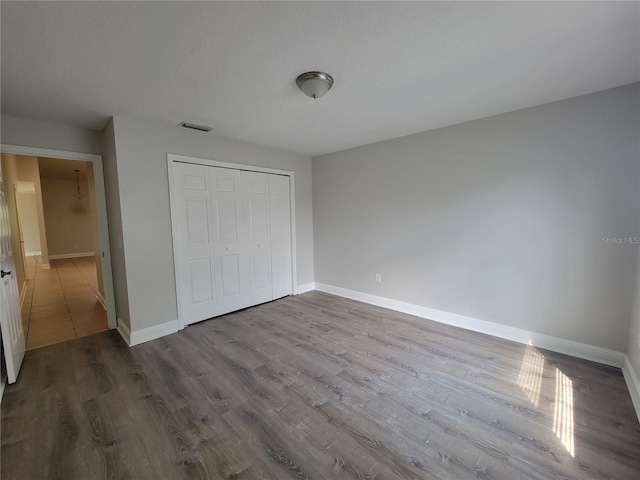 unfurnished bedroom with visible vents, dark wood-style floors, baseboards, and a closet