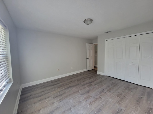 unfurnished bedroom with visible vents, wood finished floors, baseboards, and a closet