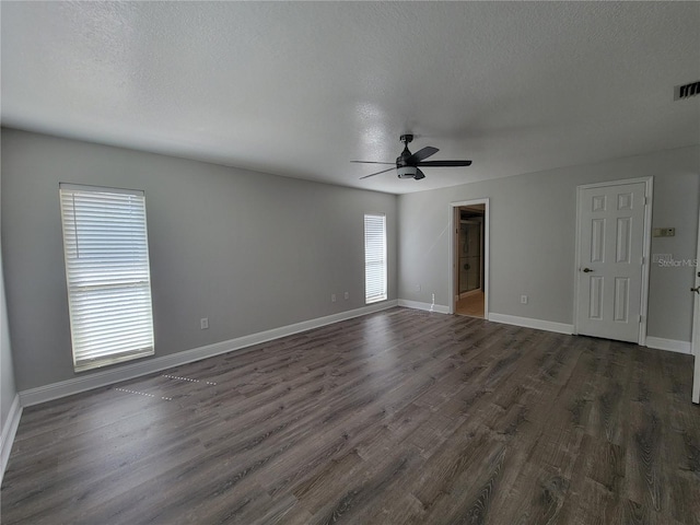 empty room with dark wood-style floors, visible vents, a textured ceiling, and baseboards