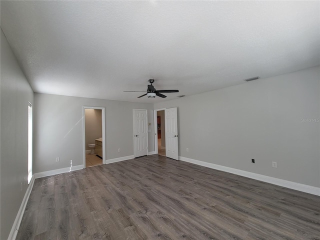 empty room featuring a ceiling fan, dark wood-style floors, visible vents, baseboards, and a textured ceiling