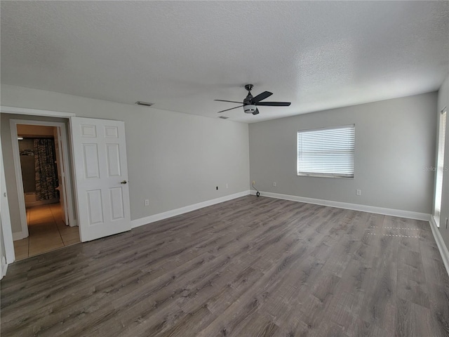 empty room with a ceiling fan, baseboards, wood finished floors, visible vents, and a textured ceiling