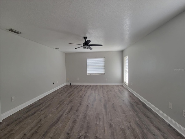 unfurnished room with a textured ceiling, visible vents, dark wood-style flooring, and baseboards