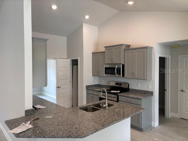 kitchen with sink, gray cabinets, appliances with stainless steel finishes, high vaulted ceiling, and kitchen peninsula