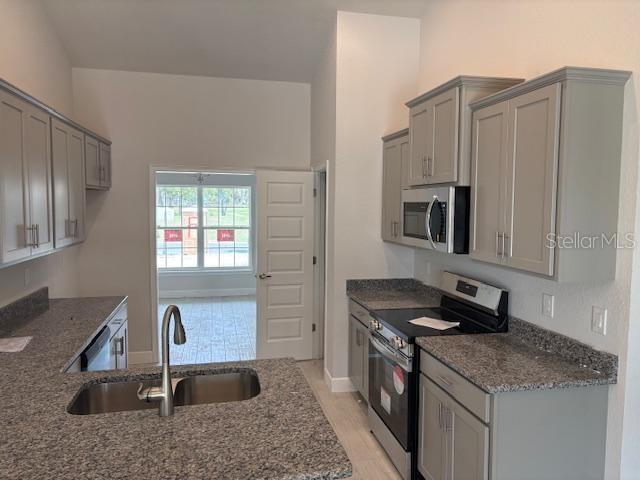 kitchen featuring stainless steel appliances, sink, dark stone countertops, and gray cabinetry