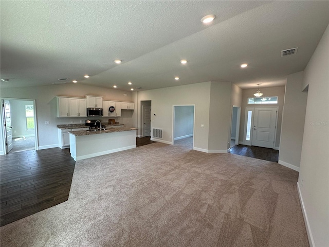 unfurnished living room with sink, a textured ceiling, an island with sink, dark stone counters, and white cabinets