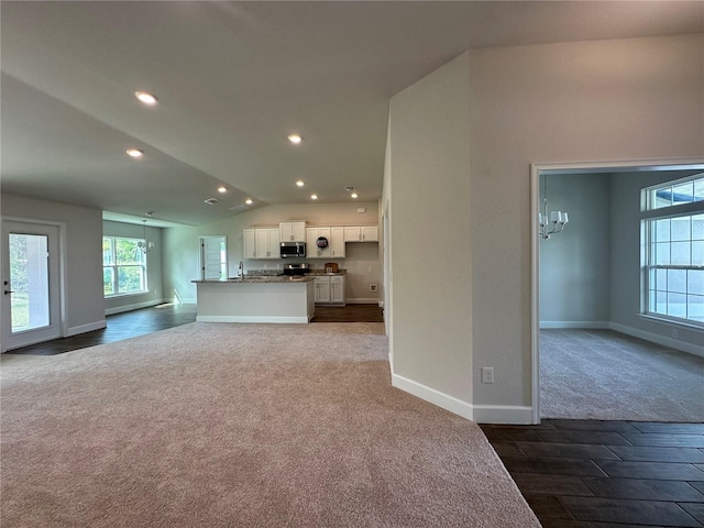 unfurnished living room featuring dark carpet, sink, and vaulted ceiling