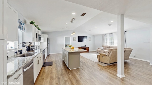 kitchen with sink, light stone counters, a kitchen island, stainless steel appliances, and white cabinets