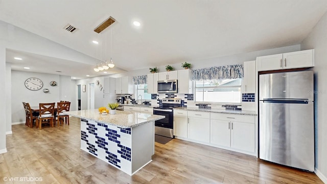 kitchen featuring pendant lighting, lofted ceiling, appliances with stainless steel finishes, white cabinetry, and a center island