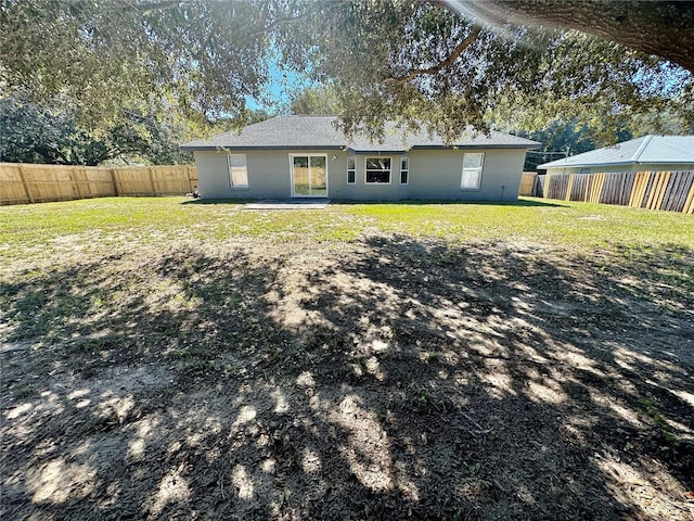 rear view of property with a fenced backyard, a lawn, and stucco siding