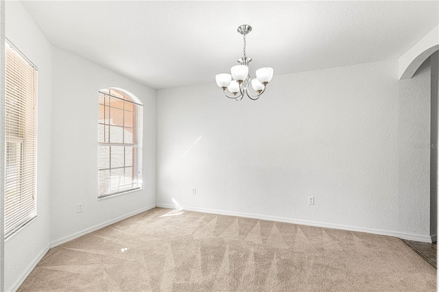 carpeted empty room with an inviting chandelier