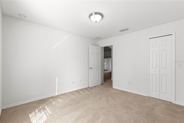 unfurnished bedroom featuring light carpet, a closet, and a textured ceiling