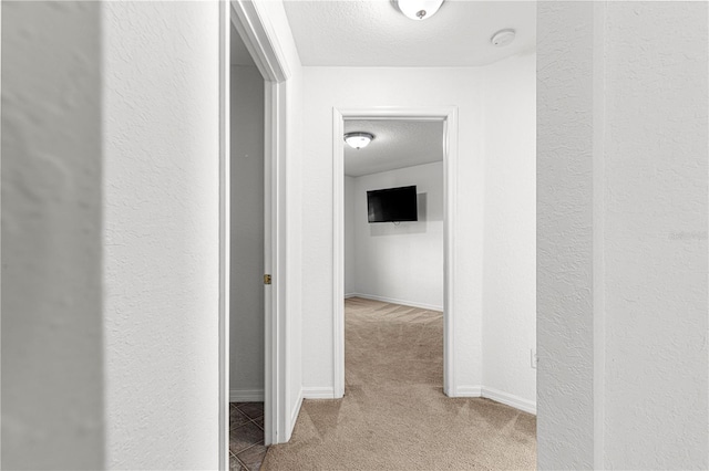 hallway with light colored carpet and a textured ceiling