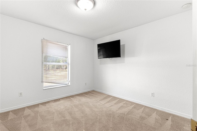 spare room featuring light colored carpet and a textured ceiling