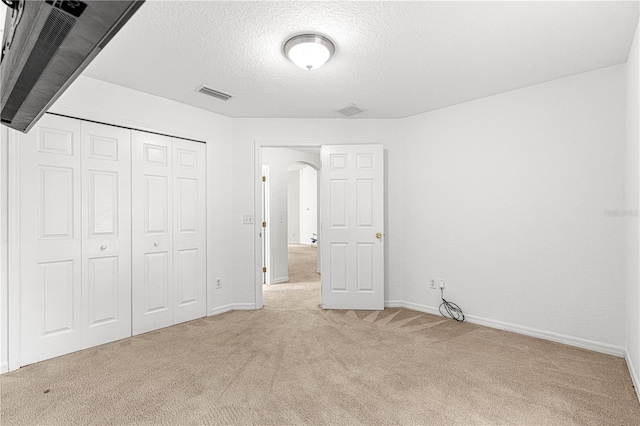 unfurnished bedroom with light colored carpet, a textured ceiling, and a closet