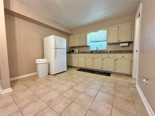 kitchen with light tile patterned flooring, stone countertops, sink, white fridge, and cream cabinetry