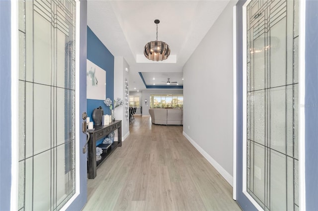 hallway featuring a tray ceiling, light hardwood / wood-style flooring, and a notable chandelier