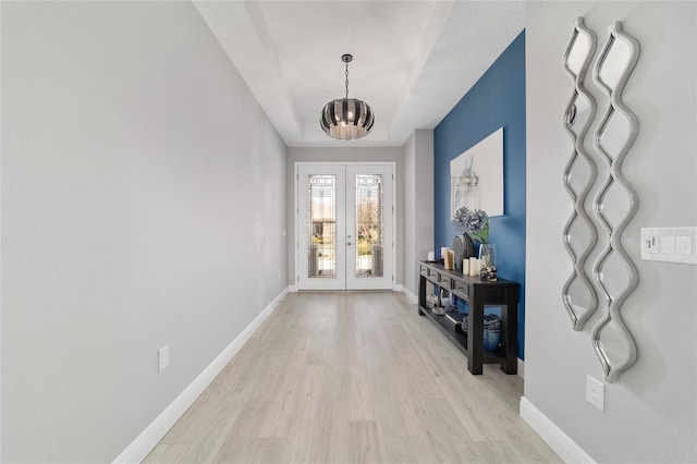 foyer entrance with a chandelier, light hardwood / wood-style flooring, french doors, and a raised ceiling