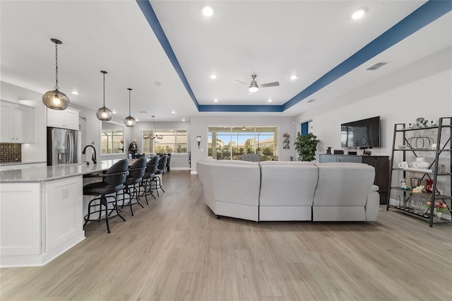 living room with sink, a tray ceiling, light hardwood / wood-style flooring, and ceiling fan