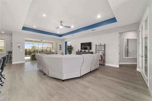 living room with a raised ceiling, ceiling fan, and light hardwood / wood-style flooring