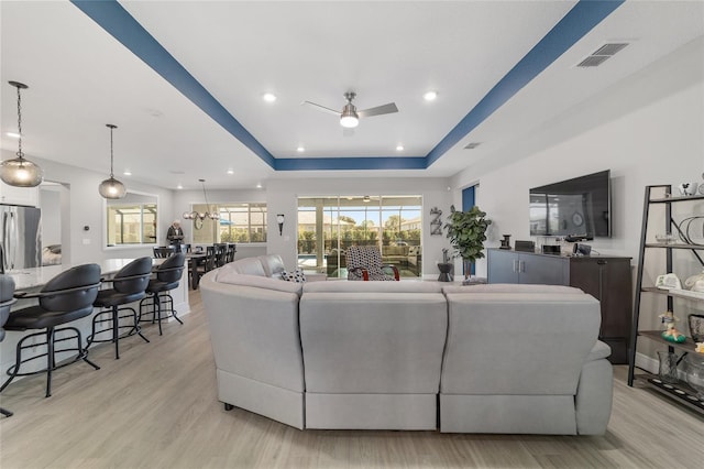 living room featuring a raised ceiling, ceiling fan, and light wood-type flooring