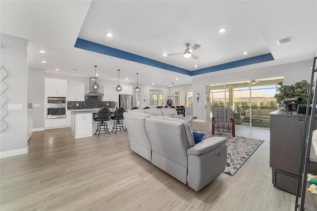 living room featuring a tray ceiling, light hardwood / wood-style flooring, and ceiling fan